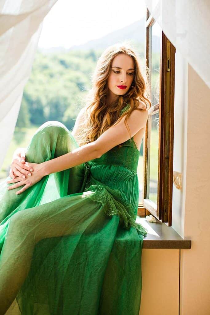 women-photoshoot-with-red-curly-hair-woman-in-flowy-green-dress-sitting-by-window-sill-by-london-professional-photographer
