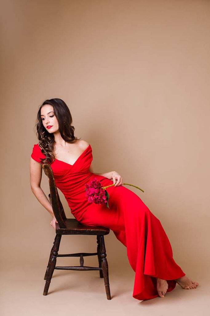 girl-sitting-on-chair-holding-red-flowers-wearing-godiva-red-evening-fishtail-dress-bare-feet-belgravia-london-photo-studio