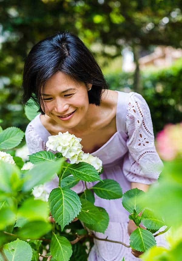 Portrait-photographer-london-Belinda-Burton-in-purple-dress-smelling-flowers-in-garden-smiling