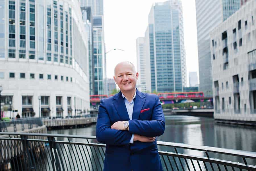 Businessman in a blue suit standing in front of modern office buildings and a canal at Canary Wharf